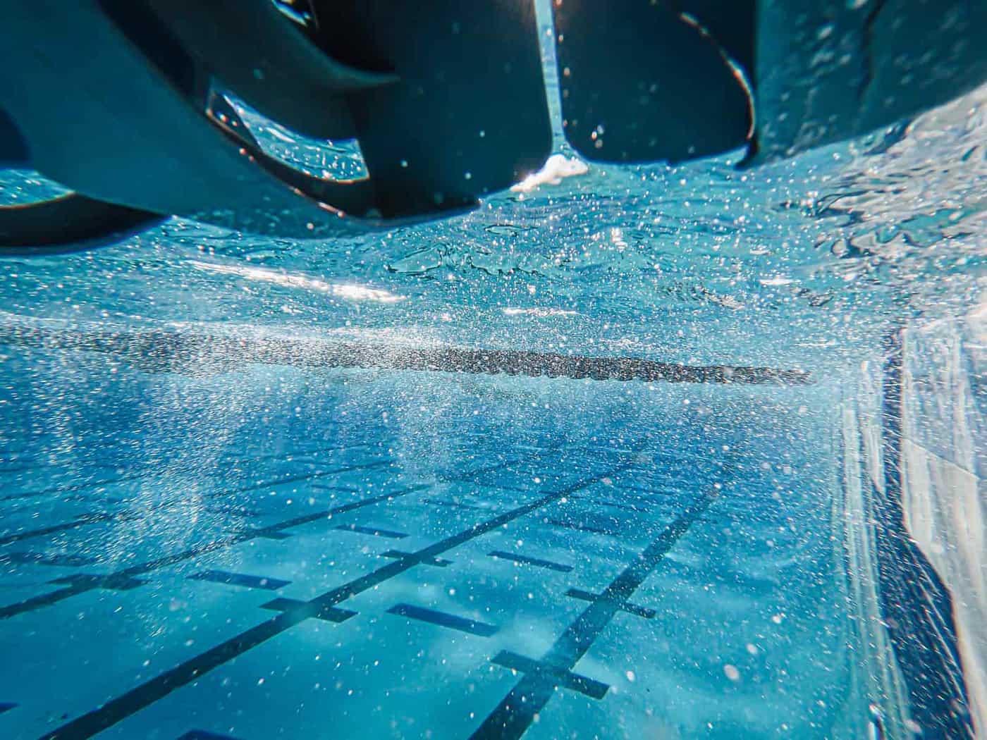 A pool wall being brushed underwater before an algaecide treatment