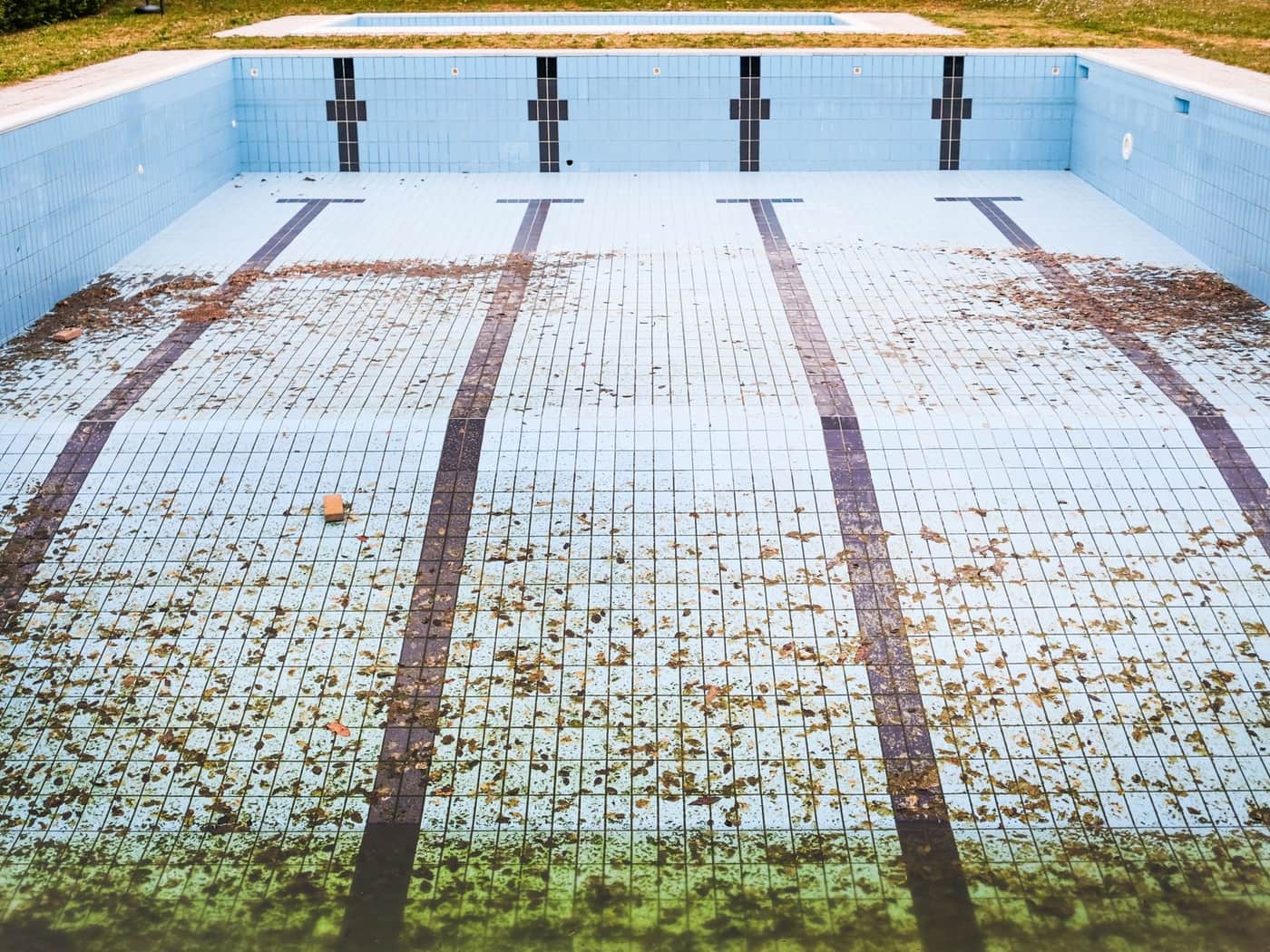 An empty swimming pool with fallen leaves scattered across the tiled floor