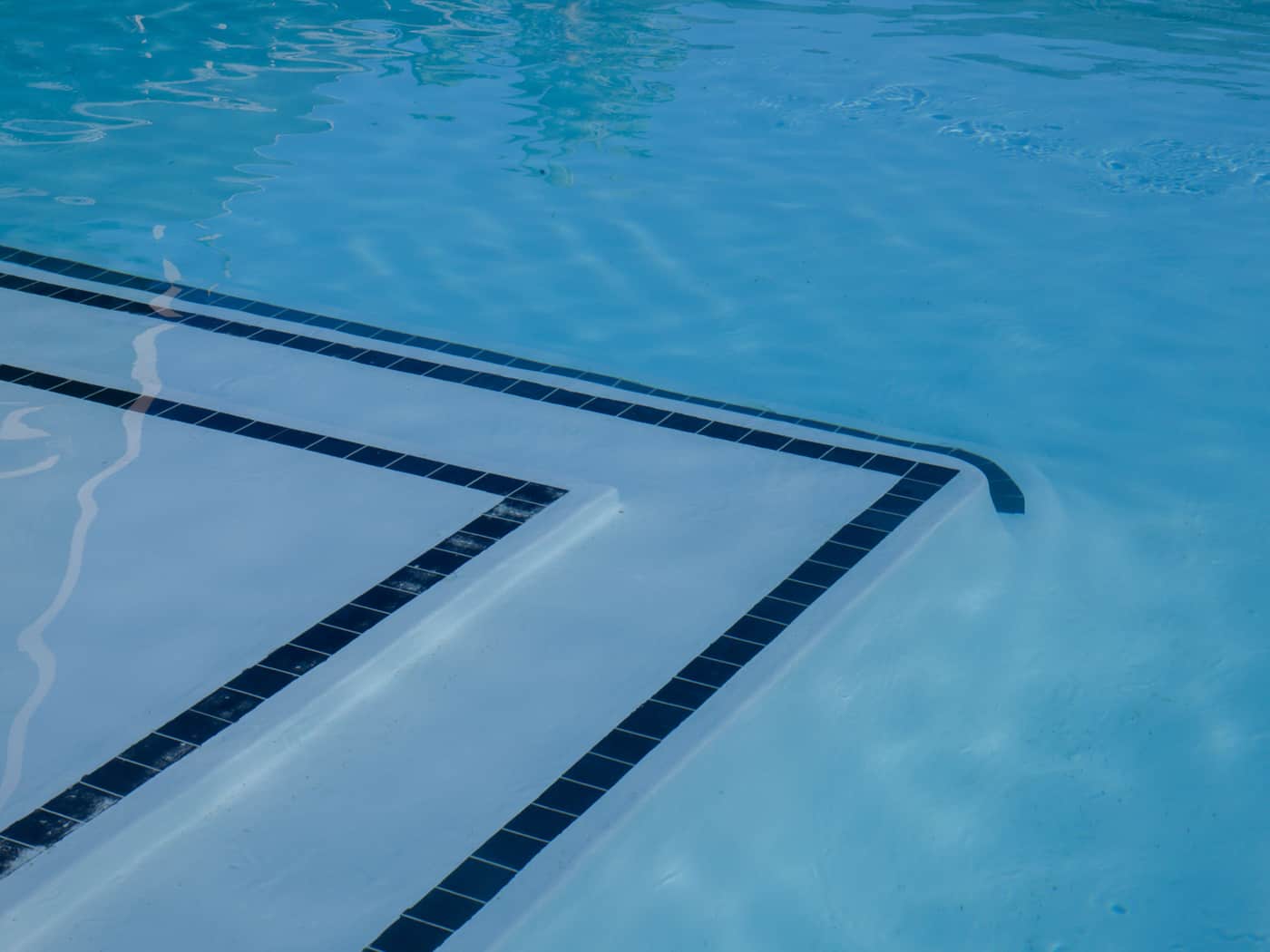 Submerged pool steps edged with dark tile on a pale in-ground pool floor
