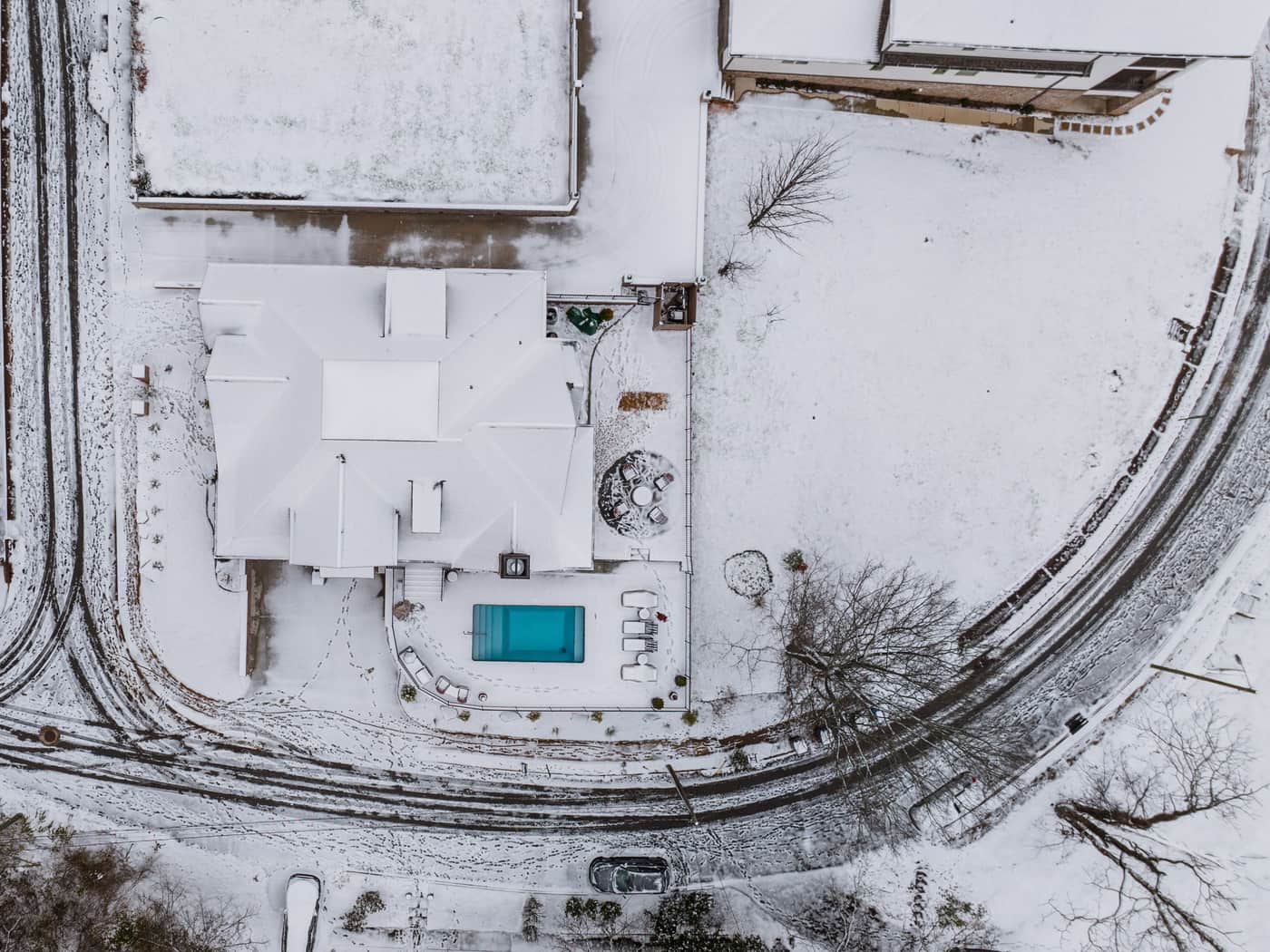 An aerial view of a snow-covered backyard with an uncovered swimming pool